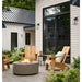 light grey round fire pit table is lit on lava rocks in front of wooden luxury chair beautifully set out in outdoor conservative