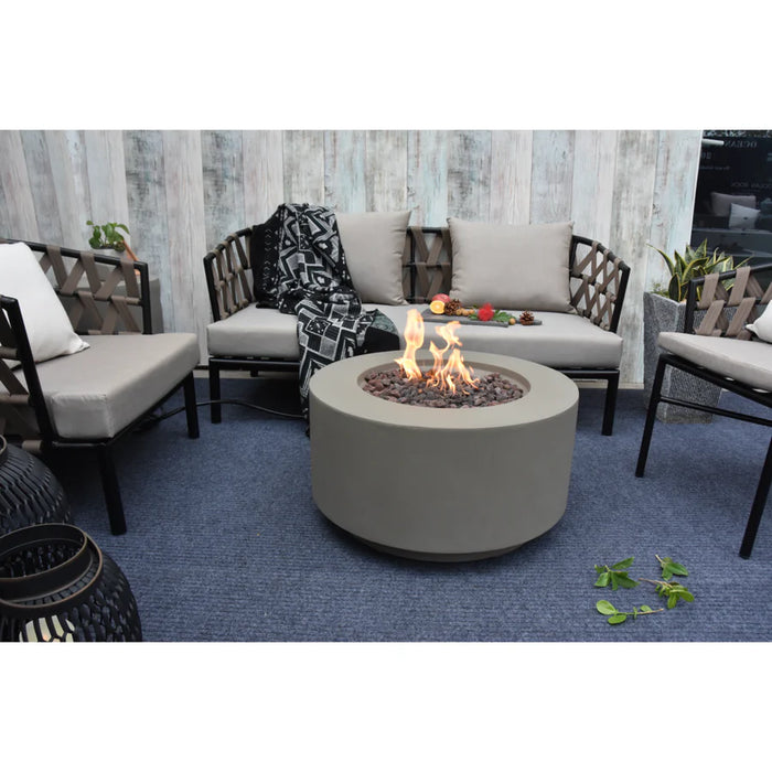 light grey round fire pit table burning on brown lava rocks inside lounge next to other furniture