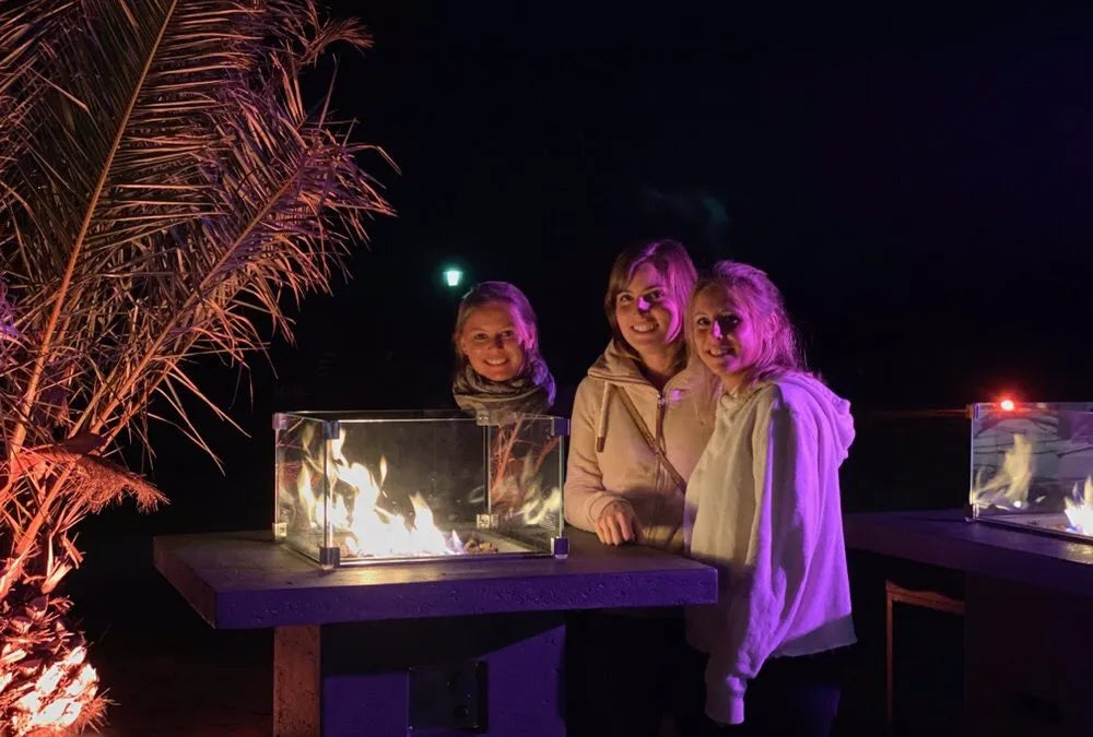 Three people sitting around a bar height fire pit table with fire displays at night