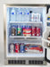  The interior of a stainless steel Fire Magic outdoor refrigerator. The refrigerator is well-stocked with various beverages and snacks, including bottles of water, cans of soda, and bags of chips. The interior is brightly lit with LED lights.