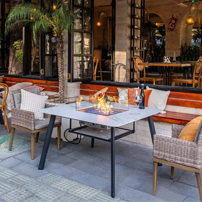 white marble outdoor dining table with glass wind screen and fire pit is lit in outdoor restaurant seating area 