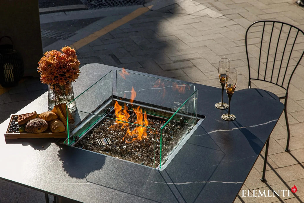 outdoor dining table with fire pit and glass windscreen with fire pit in the middle and two wine glasses on side of table