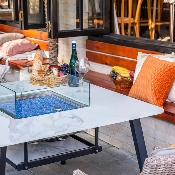 outdoor dining table with glass windscreen and blue fire glass in fire pit, fire pit is not lit