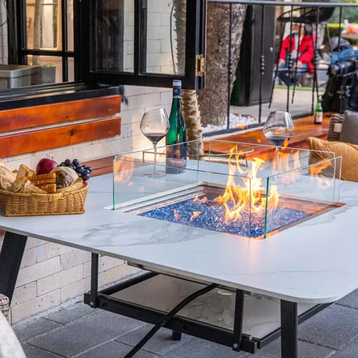 outdoor dining table with fire pit in the middle fire pit is lit on blue fire glass and have glass wind cover and table is set in outdoor restaurant 