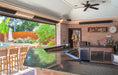 Luxurious outdoor kitchen and bar area featuring multiple patio heaters, a ceiling fan, and a view of a backyard pool.