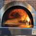 A vintage cast iron pizza oven with a red finish. The oven has a glass window in the door and a metal chimney on top. It sits on a metal stand with four legs.