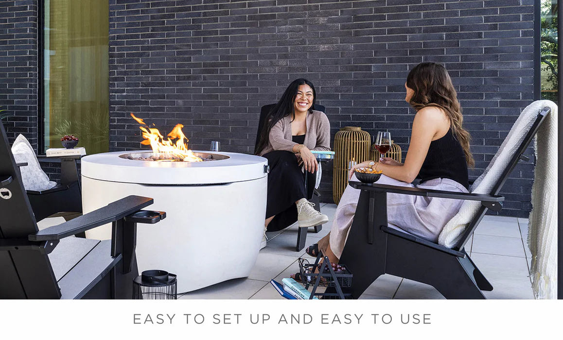 two female friends sitting around a white round propane fire pit outside and having drinks while sitting on a fire pit chair.