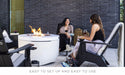 two female friends sitting around a white round propane fire pit outside and having drinks while sitting on a fire pit chair.