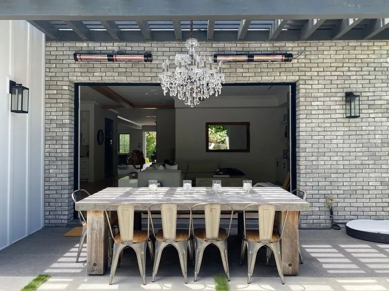 Modern outdoor dining area with a large table and chairs against a brick wall.