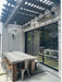 Modern outdoor dining area with a large table and chairs near a glass door.