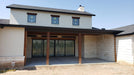 A modern house with a covered patio featuring a stone exterior and large sliding glass doors.