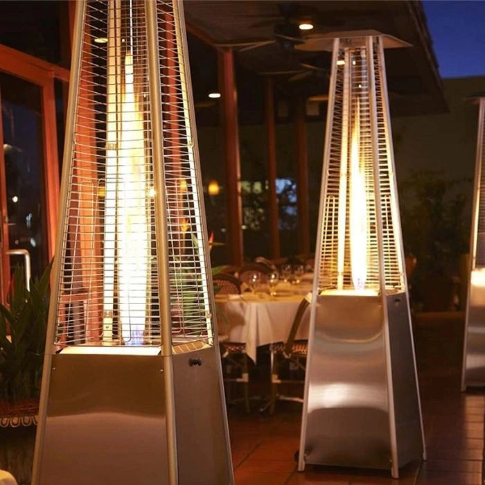 Two silver pyramid-shaped propane patio heaters with protective mesh screens, casting a warm glow over tables and chairs on a restaurant patio at night