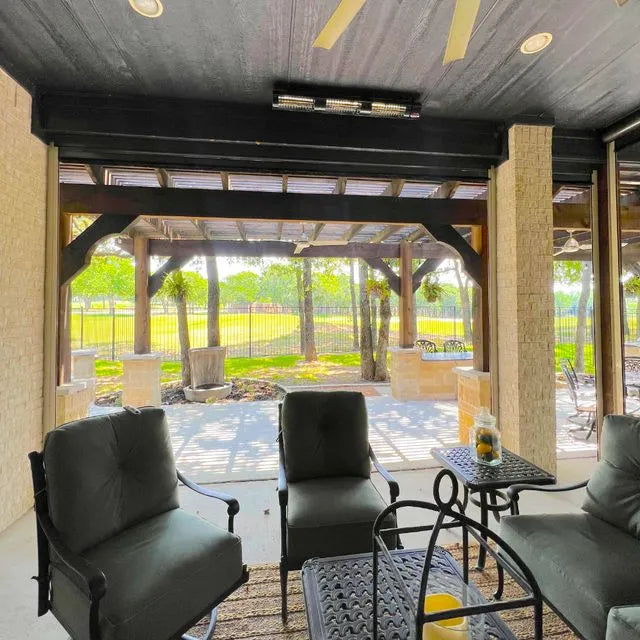 Outdoor patio area with outdoor patio electic heater mounted on the wall with black furniture and a glass wall view of a garden.