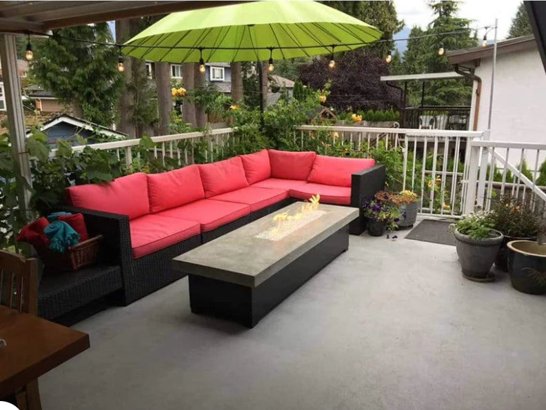 A modern outdoor patio with a comfortable couch and a rectangular fire pit. The fire pit has flames burning in it