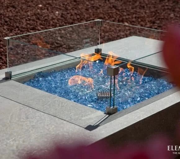 square wind screen on rectangular gas fire table. fire table is lit with orange and yellow fire on blue fire glass