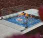 square wind screen on rectangular gas fire table. fire table is lit with orange and yellow fire on blue fire glass