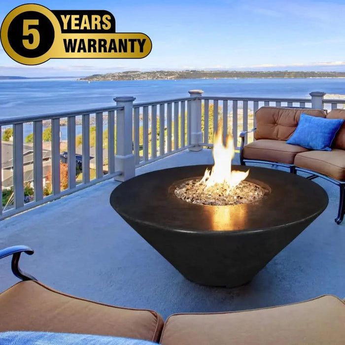 black round fire pit table with vesper black fire glass sparking in the middle of the fire pit. The fire pit is lit with yellow and orange flames. The fire pit is out on the balcony next to other outdoor furniture over  looking the sea