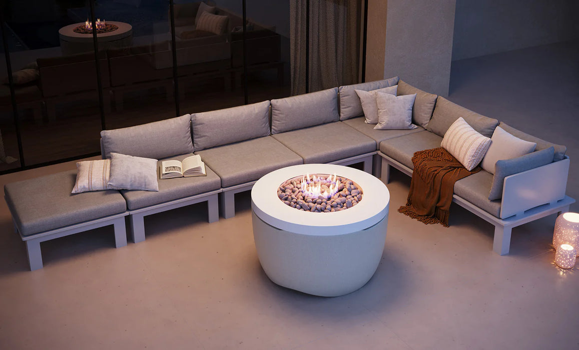 White Ledge Lounger Halo Fire Pit on a modern patio with gray sectional seating and string lights at night.