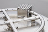 Close-up of a square, perforated metal burner attached to a round, metal ring with small holes, on a gray surface.