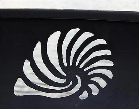 A close-up of a seashell cutout in a fire pit. The seashell is white against a dark background