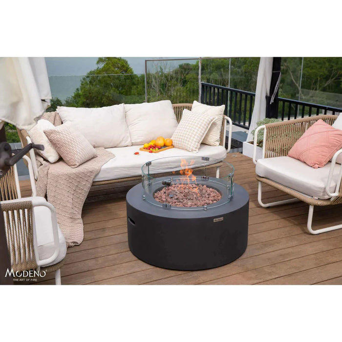 round fire pit table with glass wind screen with fire pit lit in the middle and the fire pit table is outside on the patio