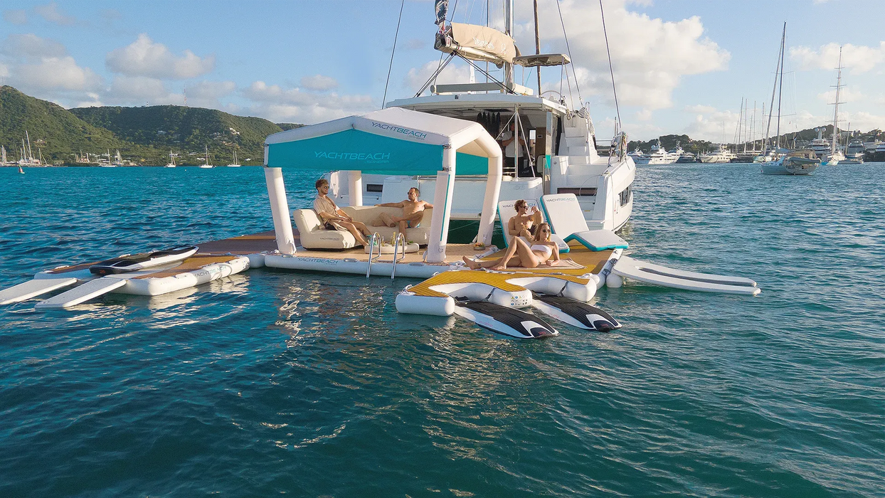 People lounging on a floating platform attached to a catamaran in the ocean.