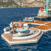 People enjoying a Yachtbeach inflatable yatch platform on a body of water with mountains in the background.