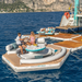 People enjoying a Yachtbeach inflatable yatch platform on a body of water with mountains in the background.