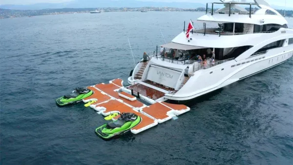 Large white yacht docked at a floating jet ski platform with water and sky in the background