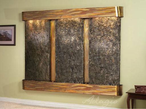 
A wide, horizontal wall-mounted water fountain with a dark, textured stone back panel divided into three vertical sections by lighter, possibly copper, columns. The top and bottom of the fountain are framed by thick, rustic-looking wooden beams with a wavy or textured pattern. 