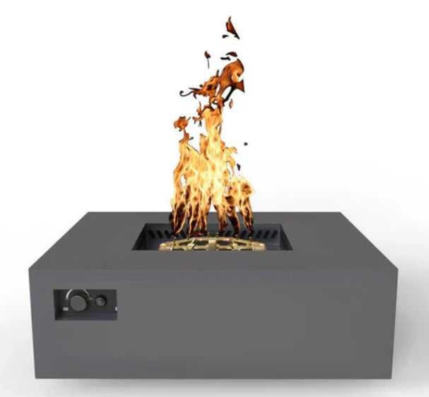 A front view of a square gas fire pit table with a gray finish. Flames are dancing above the gold-colored burner. Controls are located on the side.
