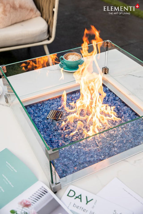 orange and yellow fire lit on white marble fire table with glass surrounding it