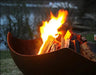 A close-up of a fire pit with flames licking at the burning wood inside. The fire pit has a unique, manta ray-shaped design.