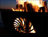 A close-up of a wood-burning fire pit at night. The fire pit has a seashell design cut into the metal. Flames are visible through the cutout.