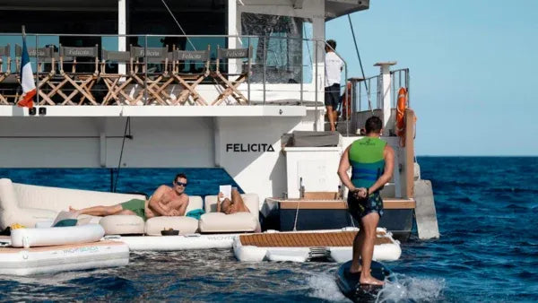 People on a luxurious yacht with 'Felicitas' branding in the ocean with a foil ramp dock attached on the edge of the boat