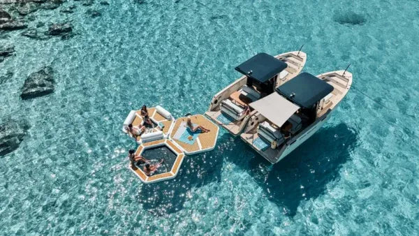 Boat with floating hexagonal pool and people enjoying the water in clear blue water.