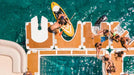 People enjoying a day at a pool party with a paddleboarder in the water.