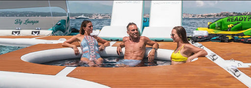 Three people relaxing in a inflatable pool attached to a yacht with a scenic background