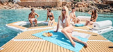 People relaxing on a sunlit dock by a pool with a scenic background