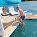 People on a Yacht Beach inflatable platform with a stainless steel dock ladder attached by a body of water
