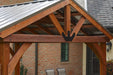 A person relaxing on a lounge chair under a wooden pavilion with a bronze-colored steel roof. The pavilion has open sides and a brown stained wood frame.