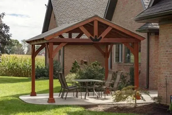 Wooden pavilion with outdoor furniture and fire pit under gazebo in front of a brick house
