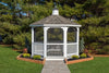 A full view of a white vinyl octagon gazebo with a gray shingle roof, surrounded by trees and landscaping.