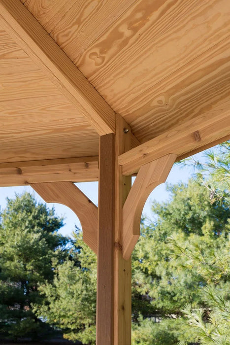 A person relaxing on a lounge chair inside a wooden octagonal gazebo. The gazebo has a shingled roof and open sides, with greenery visible in the background