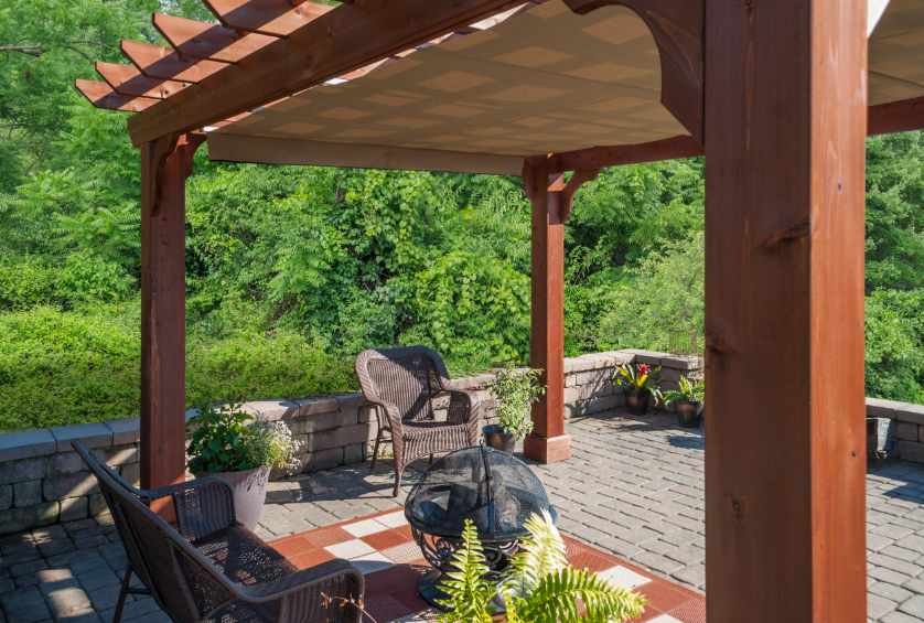 A wooden pergola with a fabric shade covering a patio with wicker furniture.