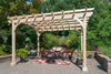 A wooden pergola with a curved top stands in a lush green backyard. It provides shade over a seating area with chairs, a small table, and a fire pit. Let me know if you'd like me to adjust this description further!